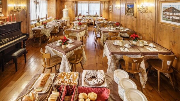 A dining hall with multiple tables set for meals, a piano, and framed artwork on the walls. - Hotel Aquila (Cortina d'Ampezzo)