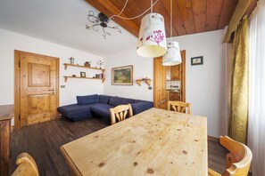 Een houten eettafel met stoelen, een blauwe bank, houten planken en een houten deur.