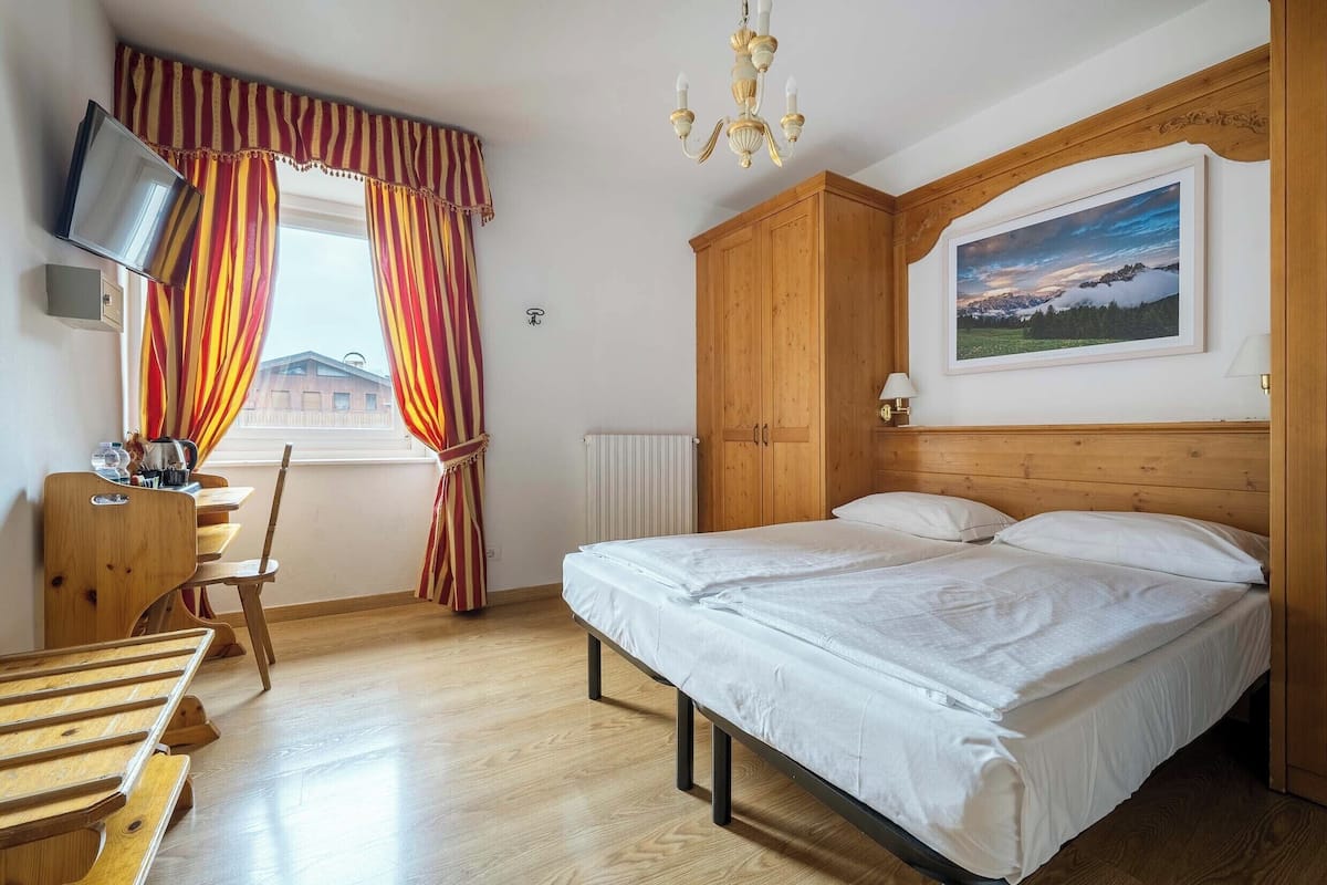 Un dormitorio con cama, armario de madera, escritorio con silla, televisor y un cuadro en la pared.