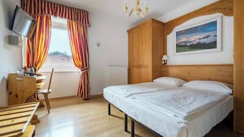 Un dormitorio con cama, armario de madera, escritorio con silla, televisor y un cuadro en la pared.