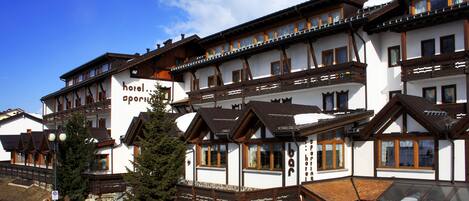 A multi-story hotel with traditional Alpine architecture, featuring wooden balconies and large windows.