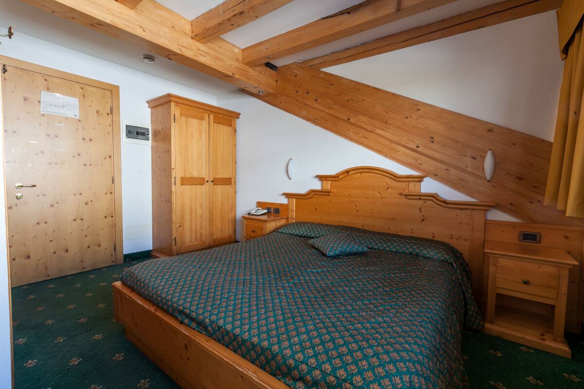 A bedroom with a wooden bed, a nightstand, a wardrobe, and a sloped ceiling.