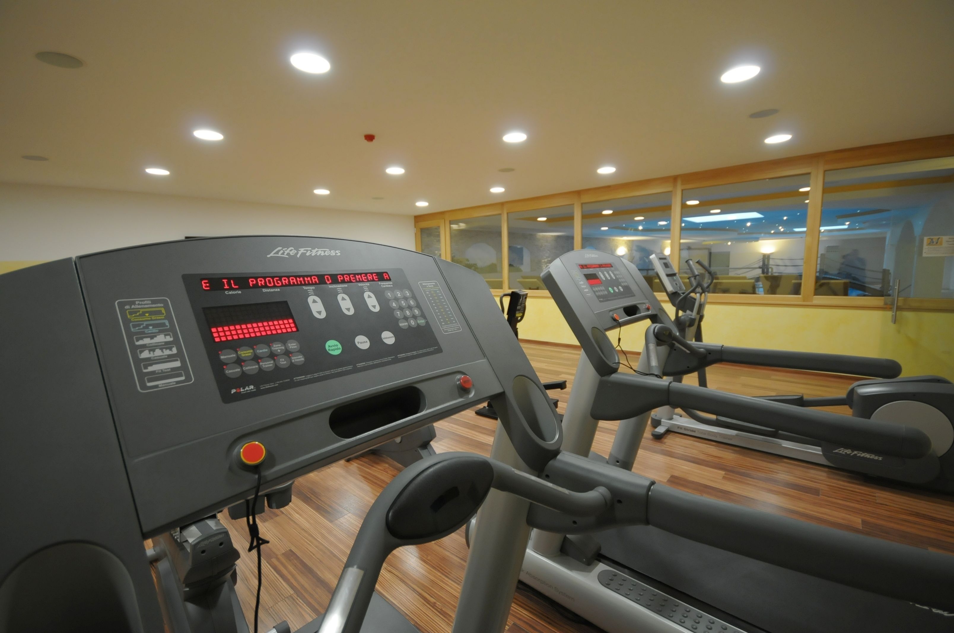 A gym with treadmills and elliptical machines, a control panel, and a window with a view of the outside.
