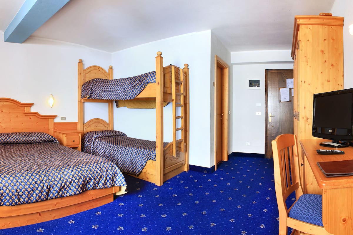A room with a bunk bed, a desk with a chair, a television, and a lamp.