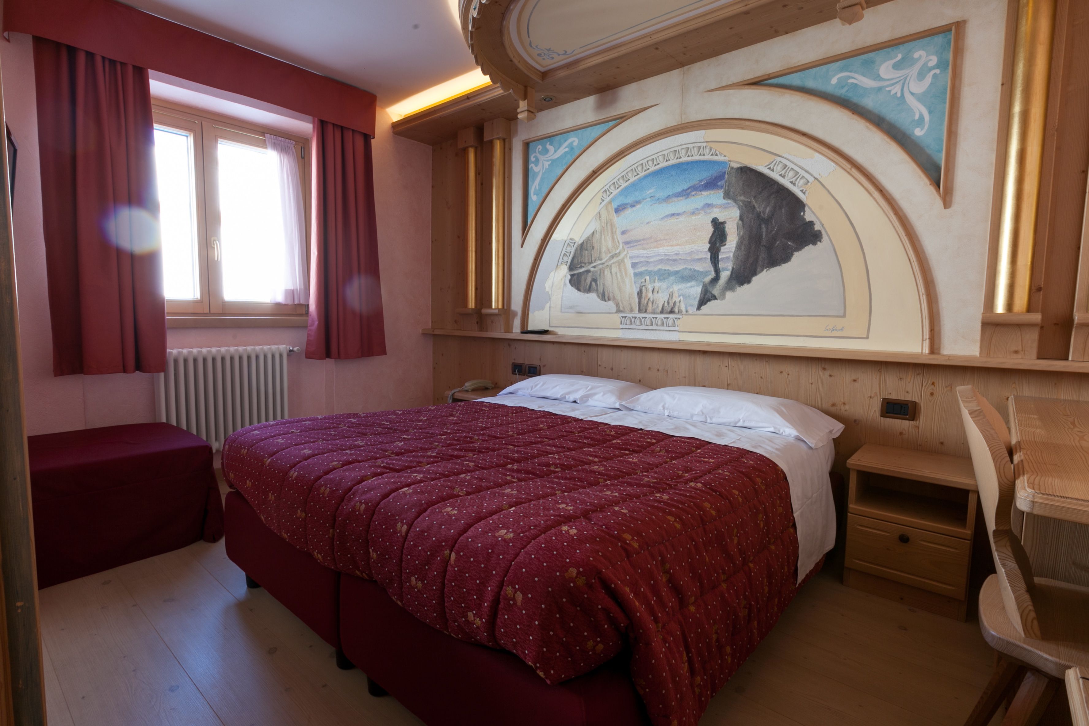 A bedroom with a large bed, a nightstand, a chair, a window with curtains, and a mural on the wall.