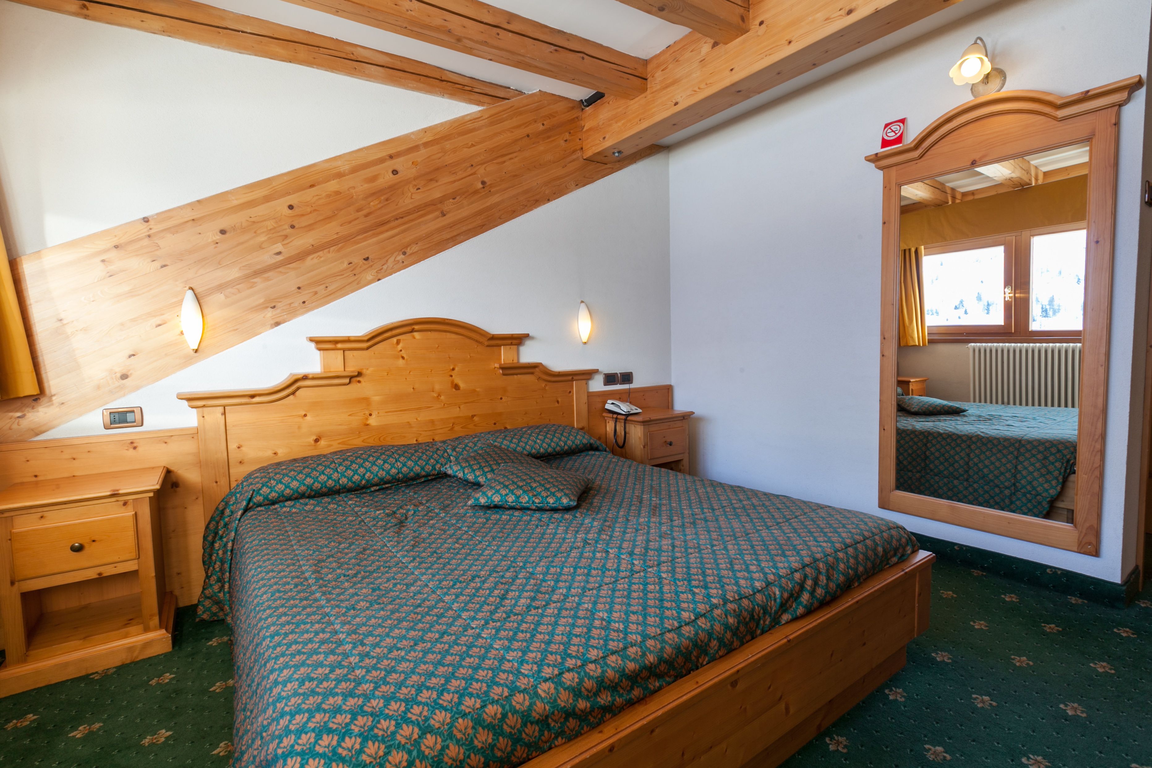 Une chambre à coucher avec un lit en bois, une table de chevet, une commode, un miroir et une fenêtre donnant sur l’extérieur.