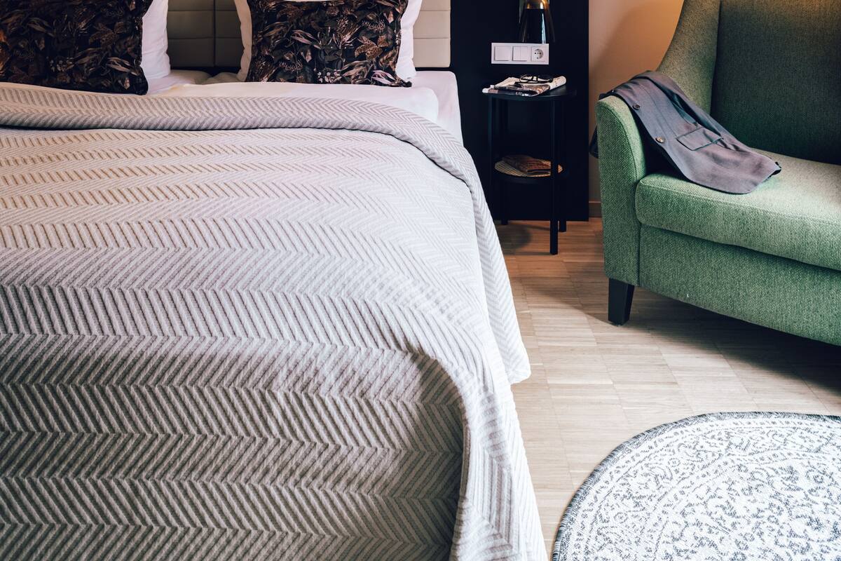 Una habitación de hotel moderna con una cama grande, un sillón verde, una mesita auxiliar pequeña y una pared decorada con notas musicales.