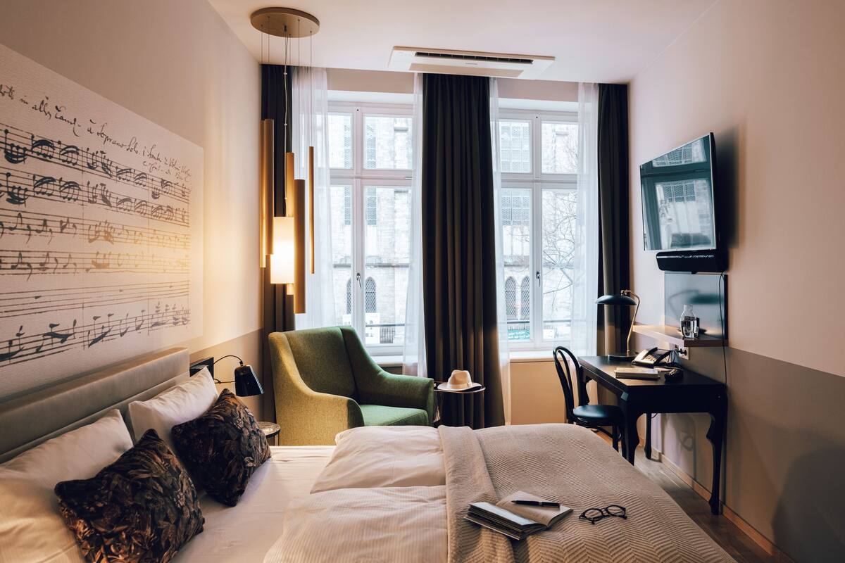 Una habitación de hotel con una cama grande, un escritorio, una silla, un televisor y una ventana con cortinas.