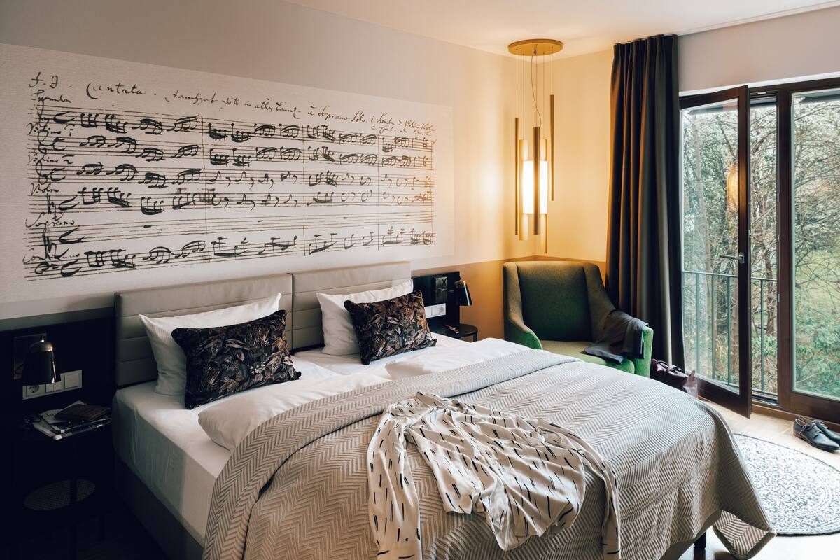 Habitación de hotel con una cama grande, una mesita de noche, una silla y una ventana con vistas a árboles.