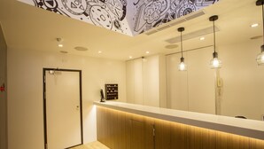 Un espace d’accueil moderne, avec un comptoir en bois, des luminaires suspendus et une fresque ornementale au plafond.