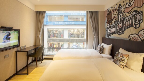 Une chambre d’hôtel avec un lit, un bureau, une télévision et une vue sur un magasin par la fenêtre.