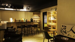 Un espace bar avec des tabourets, des étagères remplies de bouteilles et une table avec des verres.