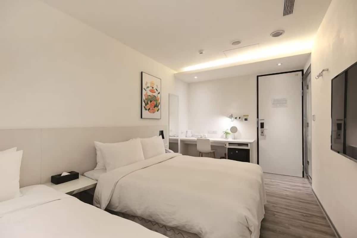 A hotel room with a bed, bedside table, desk, chair, and a door.