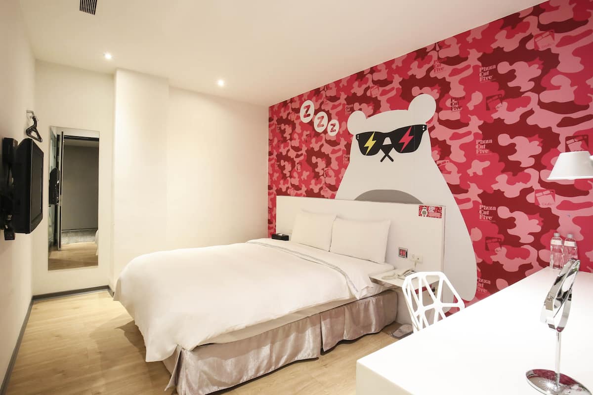 A bedroom with a bed, a bedside table, a mirror, and a wall with a red camouflage pattern and a bear graphic.