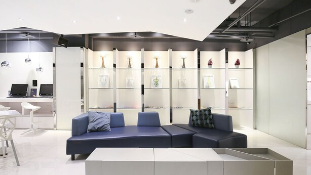 A modern interior with a sectional sofa, a glass display wall, and a white desk area.