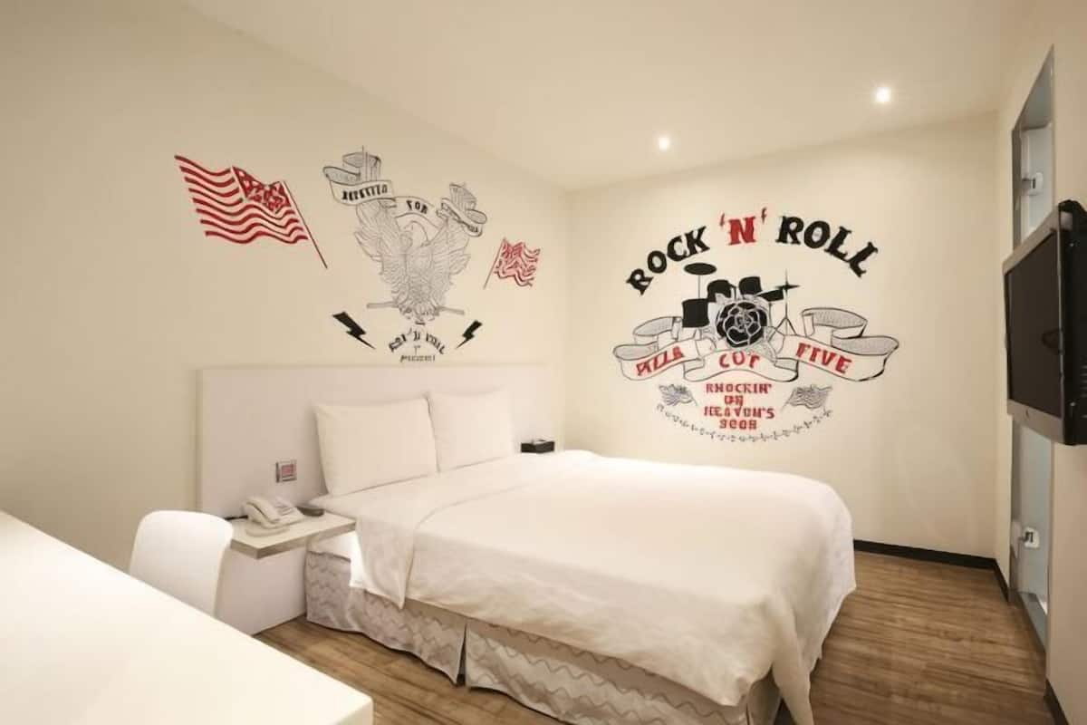 A hotel room with a bed, a nightstand, a desk, and a wall with a 'Rock 'n' Roll' mural.