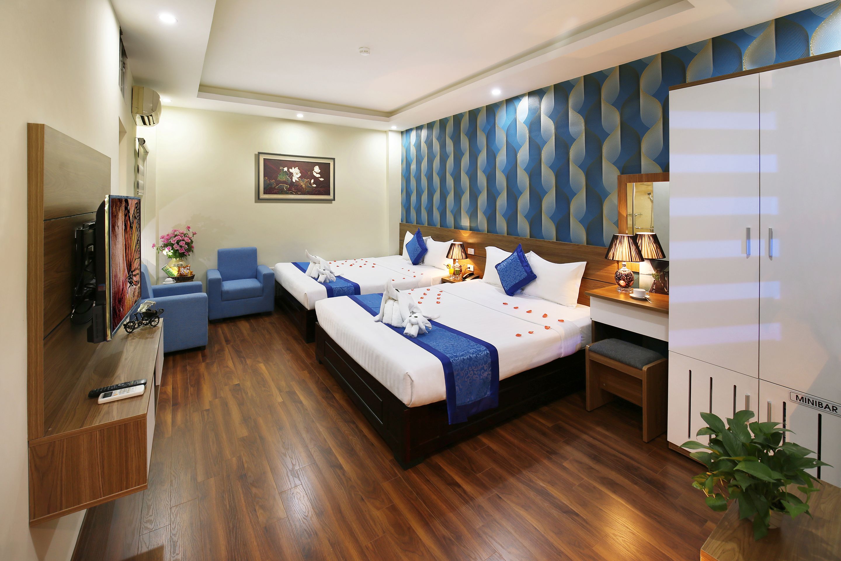 Una habitación de hotel con dos camas, televisor, minibar y zona de estar.