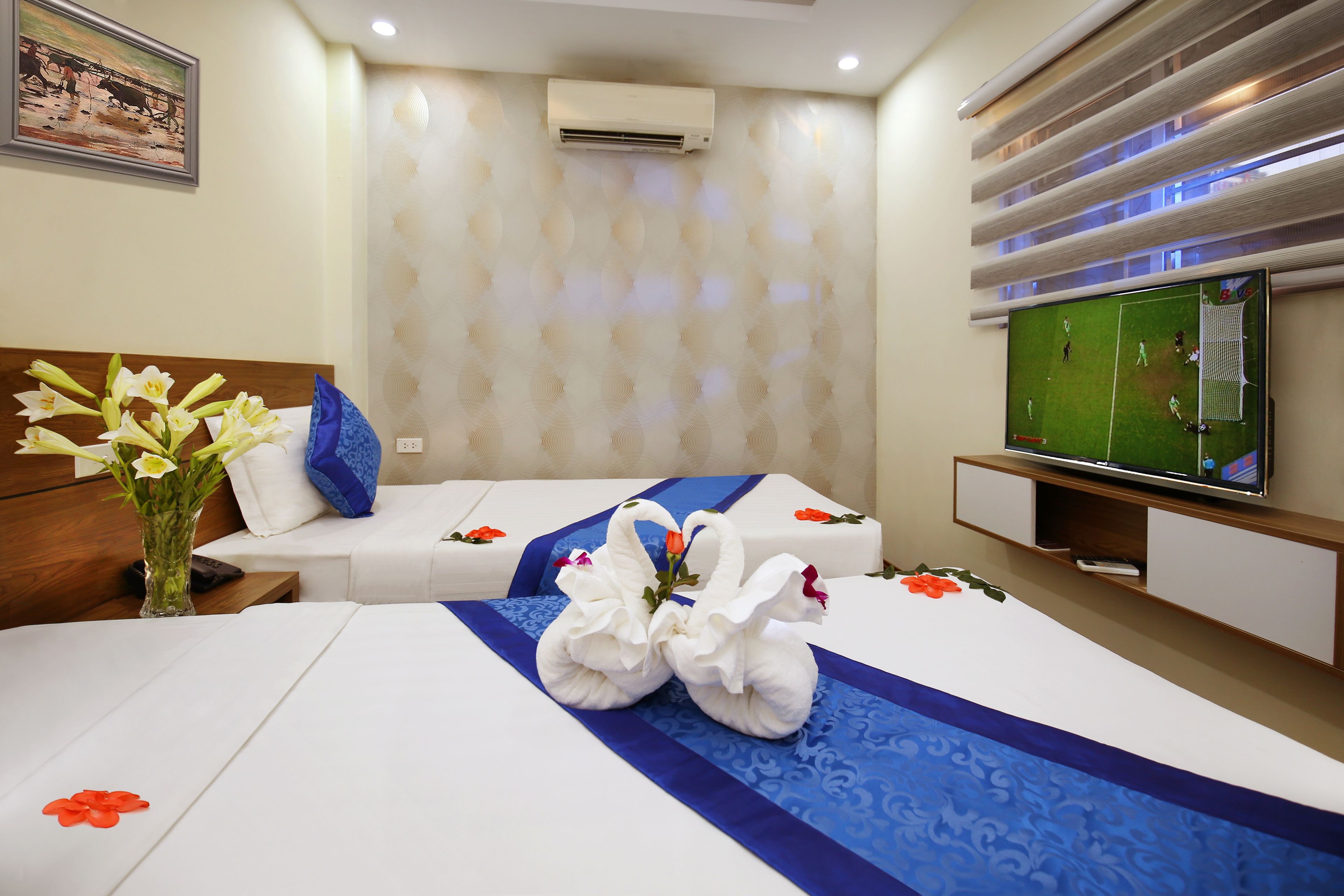 A hotel room with a bed, a TV, a vase with flowers, and a wall-mounted air conditioner.