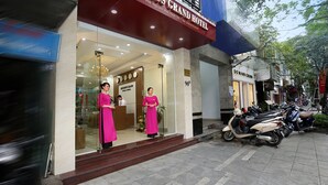 The exterior of the Aquarius Grand Hotel with a clear entrance, a reception area with two staff members, and a row of parked scooters outside. - Aquarius Grand Hotel (Hanoi)