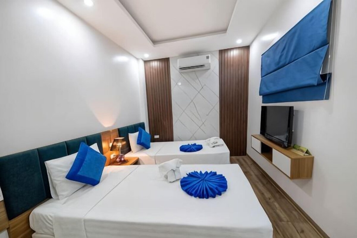 A hotel room with two beds, a television, and a window with blinds.