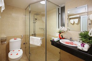 A bathroom with a glass-enclosed shower, a toilet, a sink with a mirror, and a potted plant.