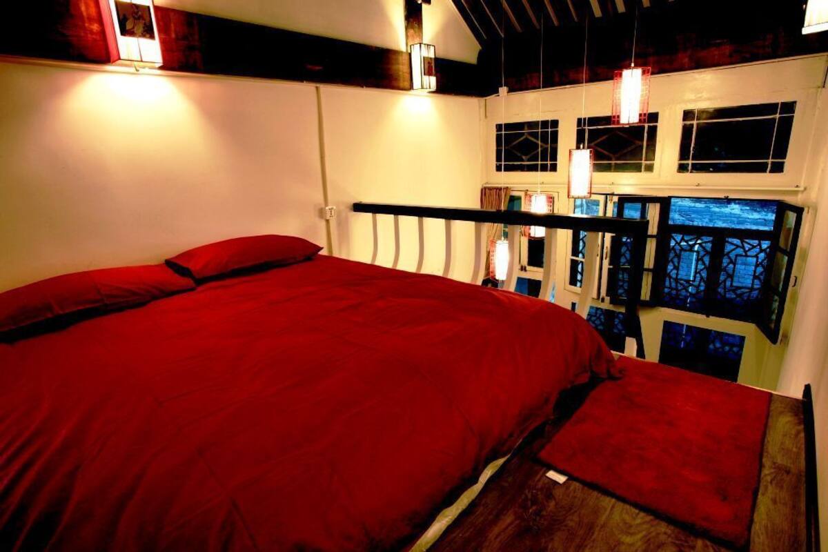 A bedroom with a large bed, a wooden headboard, and a view of the night sky through windows.