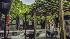 Un espacio al aire libre con pérgolas de madera, plantas en macetas y faroles rojos.