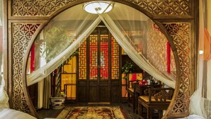 Una habitación tradicional con cama a dosel, una puerta de color rojo y dorado con motivos, y un techo de madera con diseños intrincados.