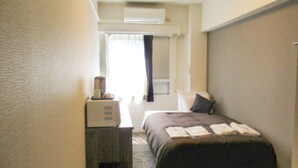 A hotel room with a bed, a desk with a lamp, and an air conditioning unit on the wall. - HOTEL LiVEMAX Kawasaki Ekimae (Kawasaki)