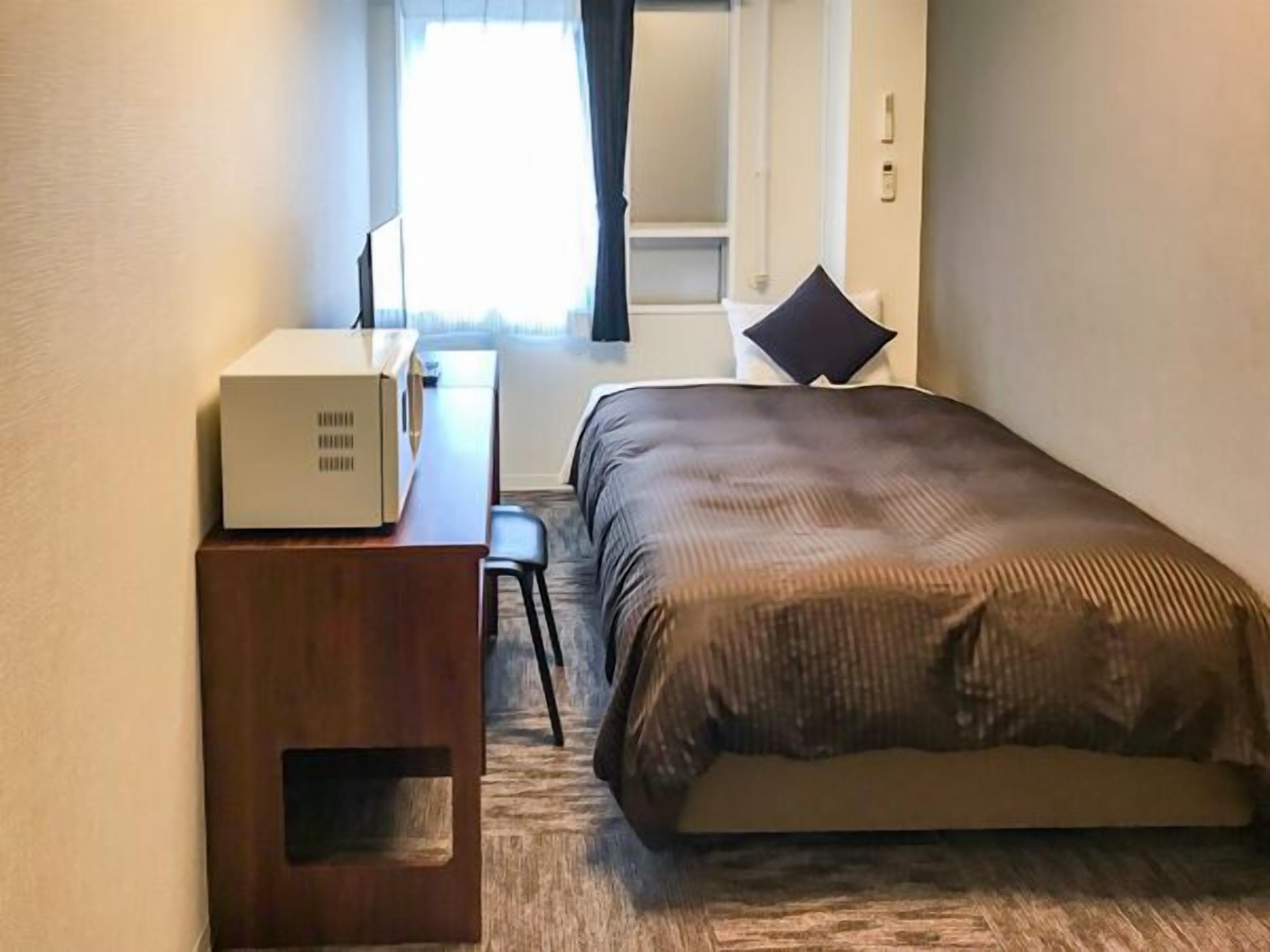 Hotellihuone, jossa on sänky, työpöytä, tuoli ja matkalaukku.