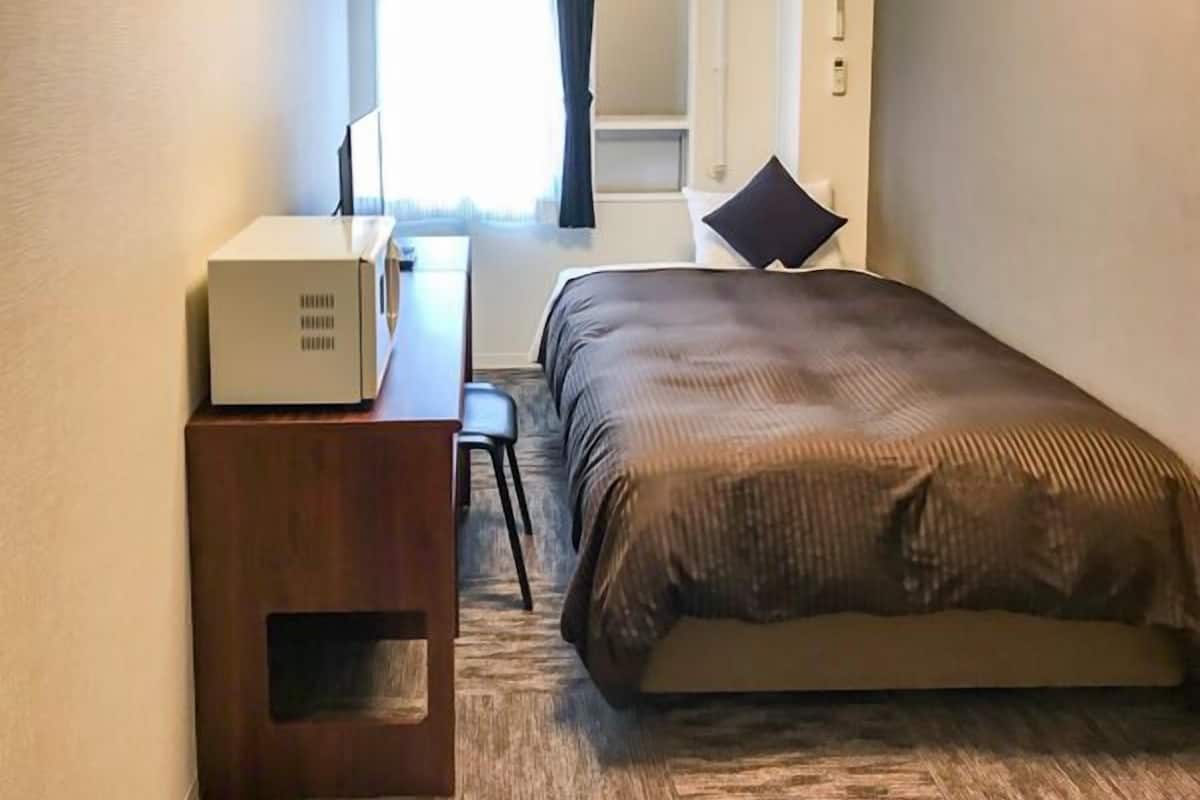 A hotel room with a bed, a desk, a chair, and a suitcase.