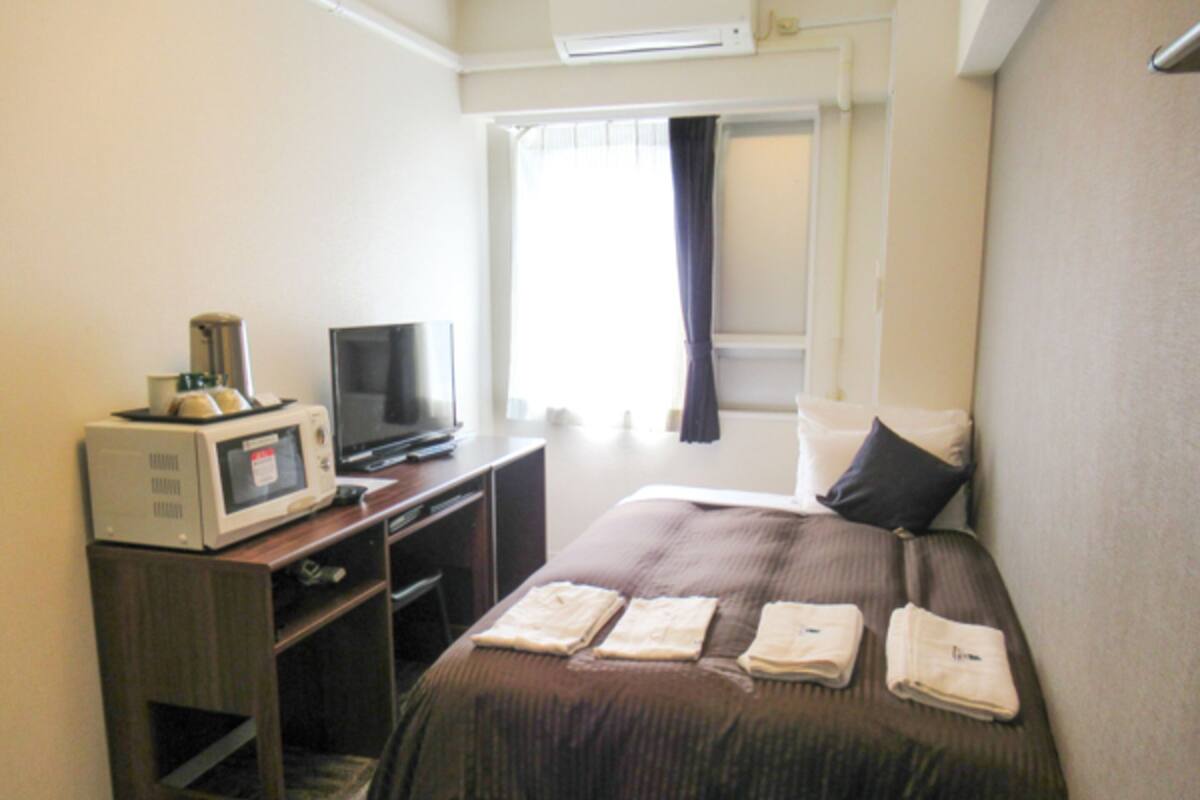 Une chambre d’hôtel équipée d’un lit, d’une télévision, d’un four à micro-ondes et d’une fenêtre avec des rideaux.