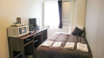 A hotel room with a bed, a television, a microwave, and a window with curtains.