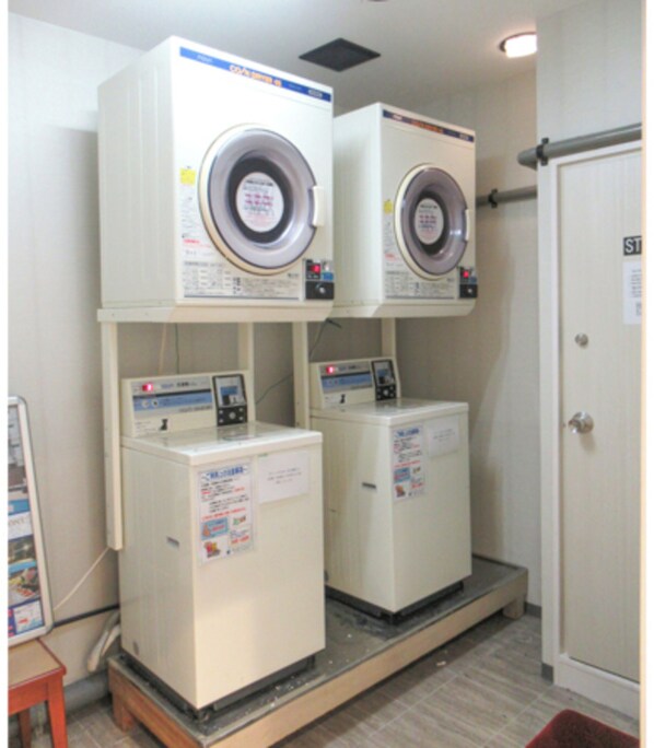 Two stacked front-loading washing machines in a laundry room with a door and a bulletin board.