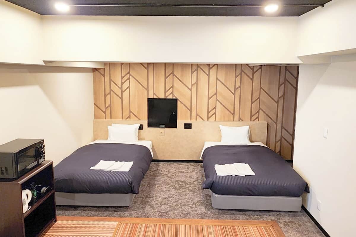 Habitación de hotel con dos camas, un televisor montado en la pared y un microondas en un estante.