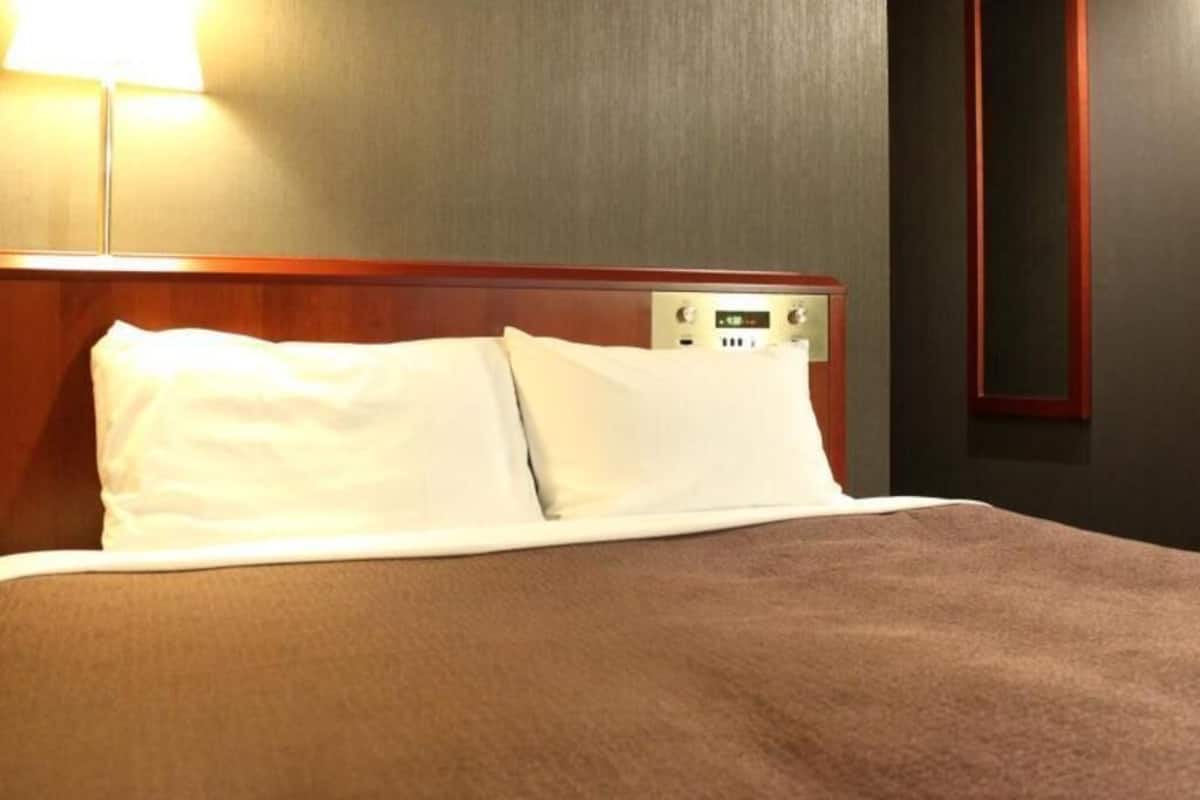 Habitación de hotel con cama, panel de control y espejo montado en la pared.