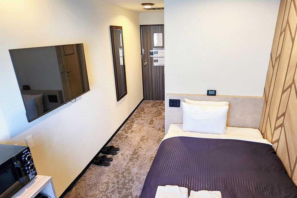 Habitación de hotel con cama, escritorio con microondas, espejo y puerta con un cartel.