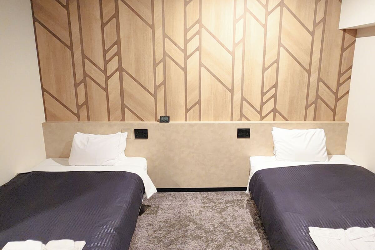 Habitación de hotel con dos camas individuales, un cabecero estampado y suelo alfombrado.