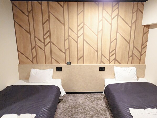Habitació d'hotel amb dos llits individuals, un panell decorat al capçal i terra amb moqueta.