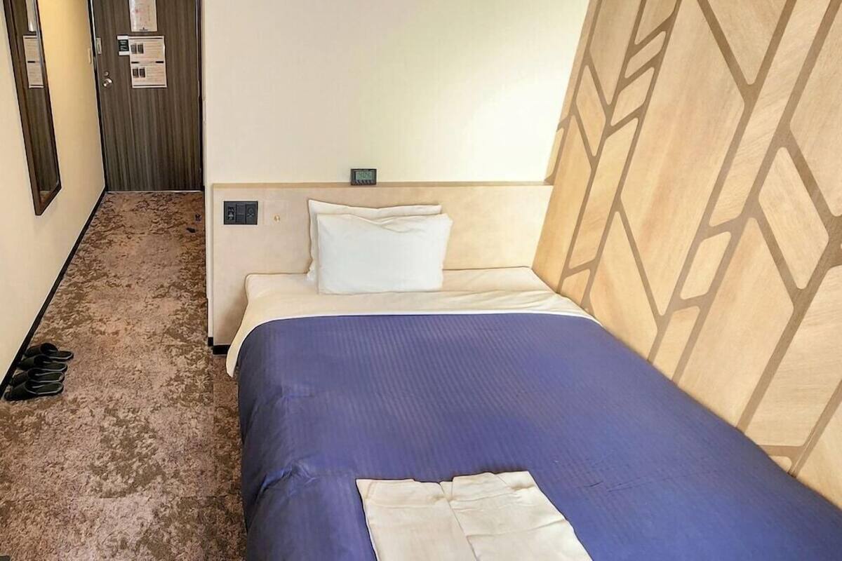 Una habitación de hotel con una cama, un cabecero de estampado geométrico, un reloj de pared y una puerta con espejo y un aviso.