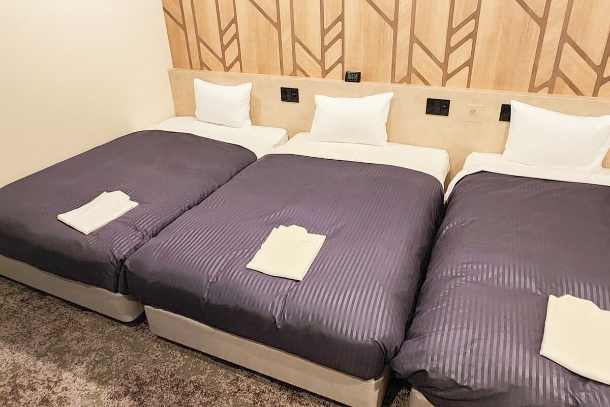 Habitación de hotel con una cama, cabecero de madera con diseño geométrico, tres almohadas y una toalla blanca doblada en cada cama.