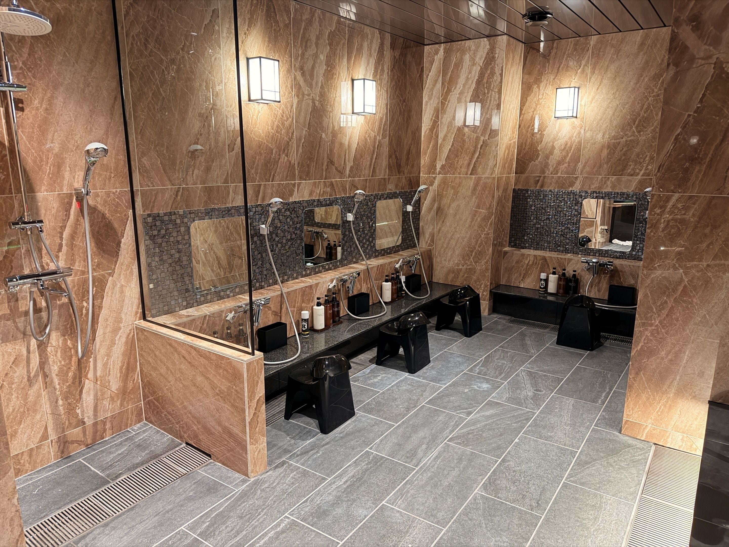 A modern bathroom with marble walls, a large mirror, a black vanity, and a shower area.