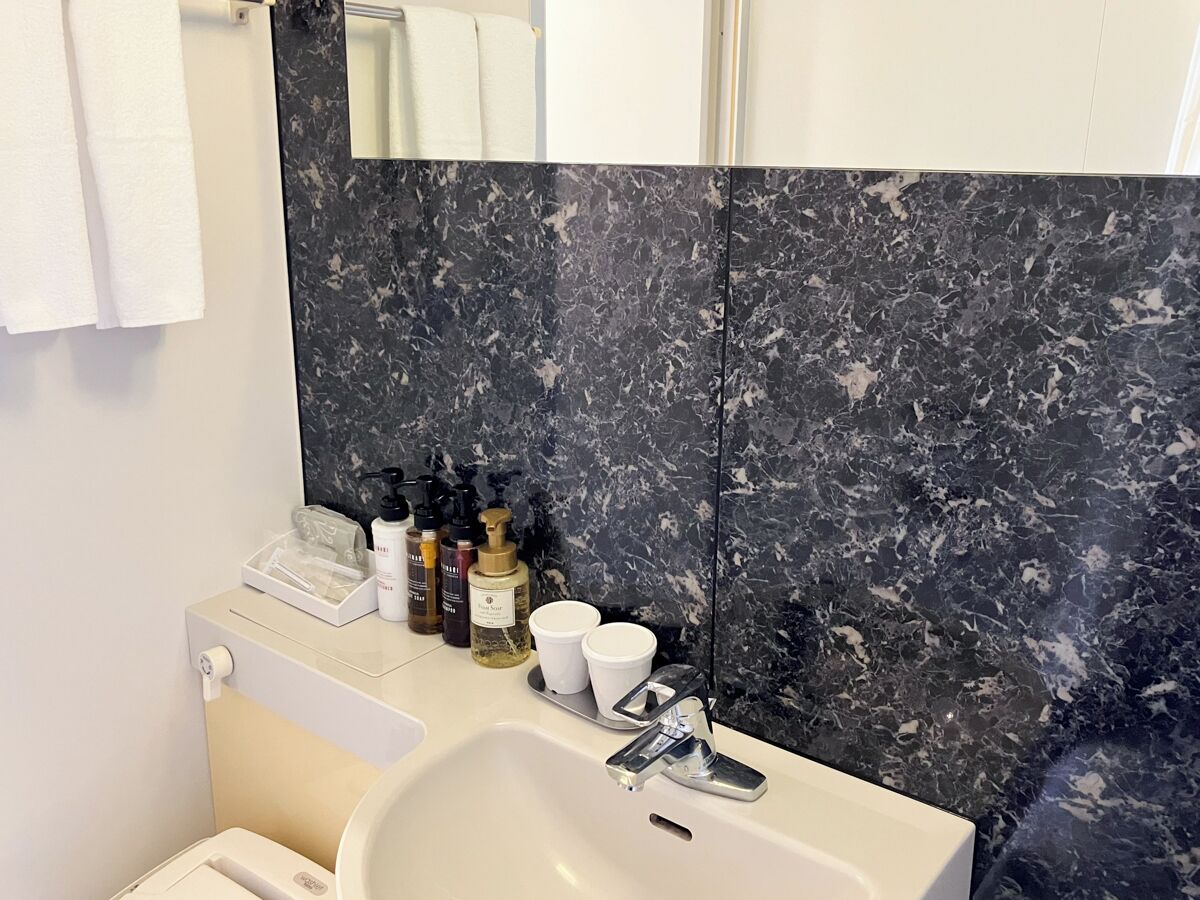 A bathroom with a marble backsplash, a sink, a mirror, and toiletries on the counter.