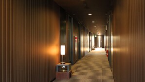 A hotel corridor with wooden panel walls, a checkered carpet, a standing lamp, and a fire extinguisher on the right wall. - HOTEL LiVEMAX Hiratsuka Ekimae (Hiratsuka)