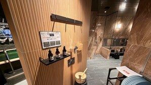 A modern bathroom with a wooden panel wall, a shelf with toiletries, a wooden bucket, and a towel rack. - HOTEL LiVEMAX Hiratsuka Ekimae (Hiratsuka)