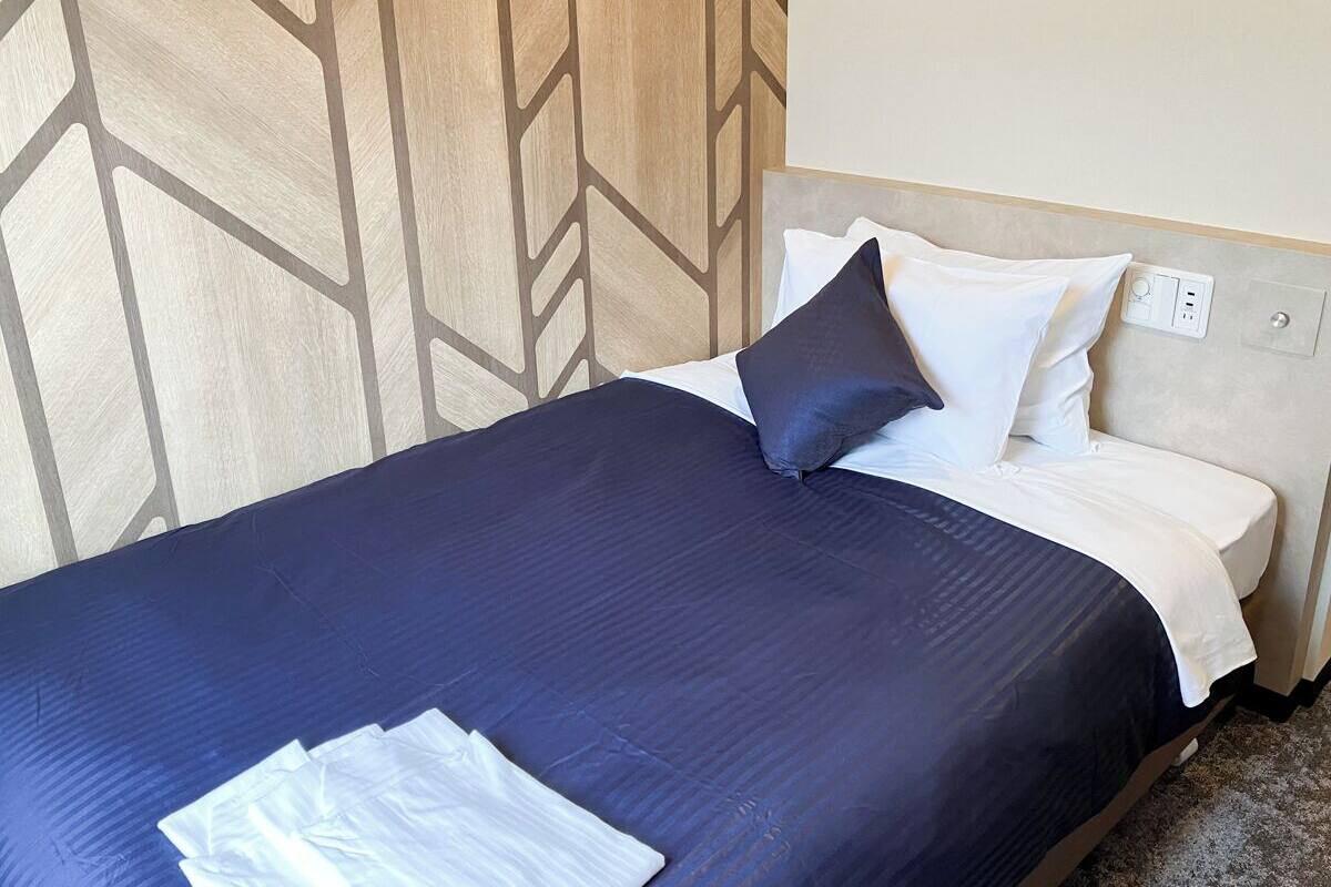 Cama bem arrumada com colcha azul escura e almofadas brancas, em frente a parede com padrão geométrico.