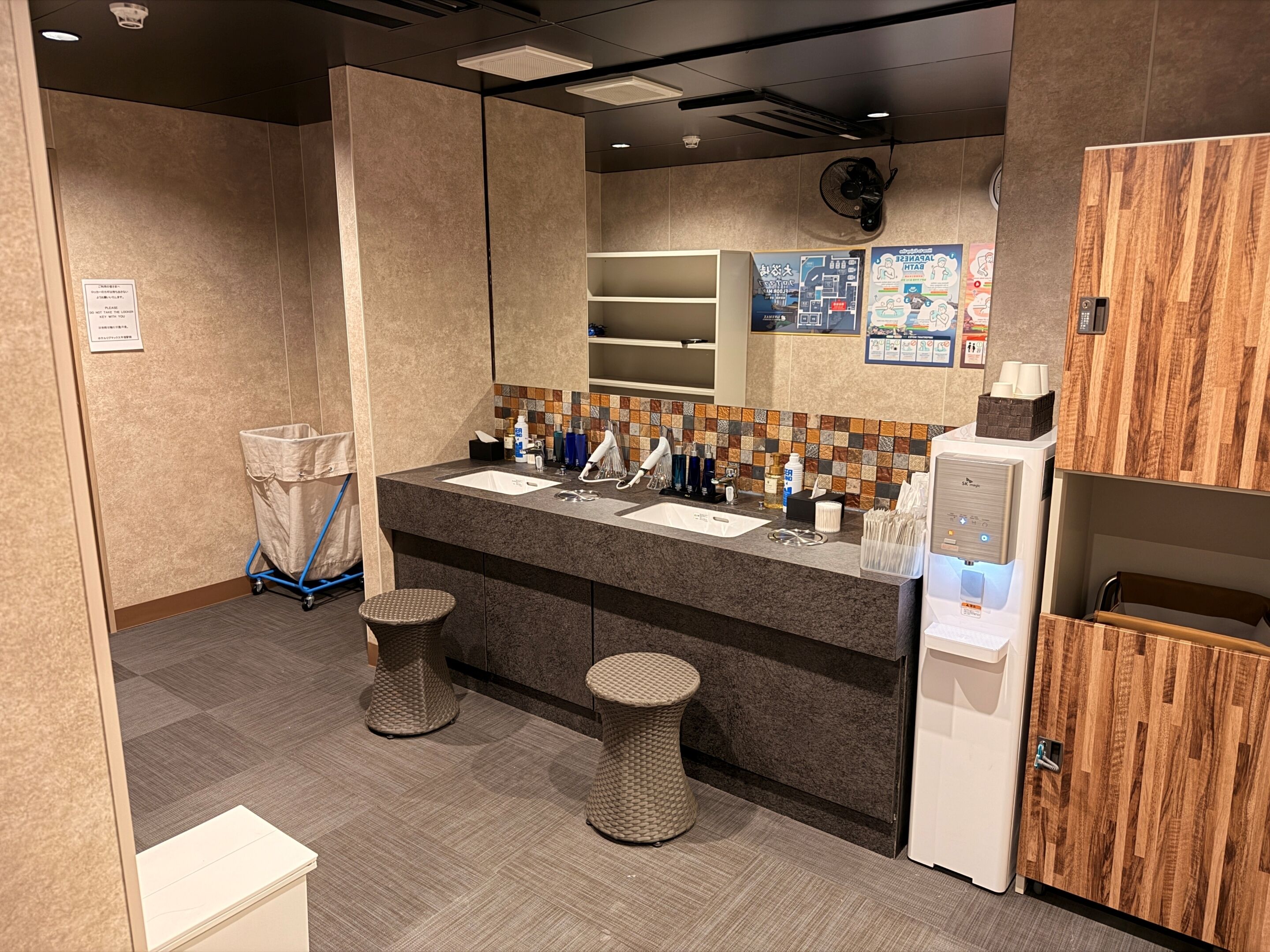 A modern bathroom with two sinks, a mirror, a fan, and a refrigerator.