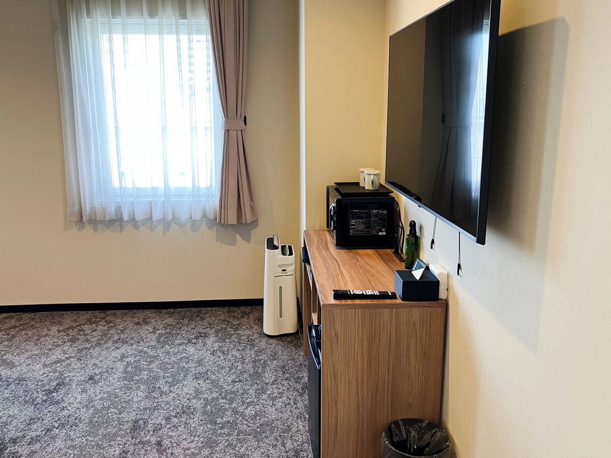 Een hotelkamer met een houten bureau, een flatscreen televisie, een koffiezetapparaat en een prullenbak.