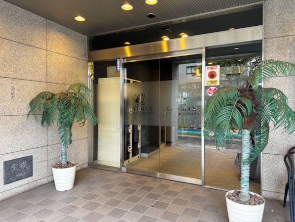 Entrada de hotel con puerta de vidrio, plantas en macetas y un letrero que indica zona para no fumadores.