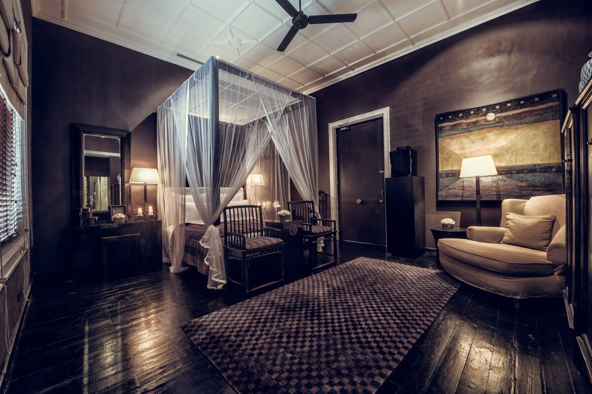 Une chambre à coucher faiblement éclairée, avec un lit à baldaquin, un canapé et un grand tableau accroché au mur.